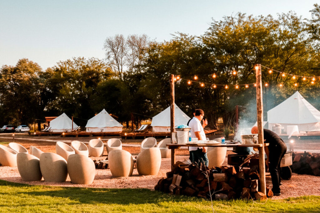Área común de cocina y parrilla al aire libre en Terranova Glamping al atardecer, con luces y asientos.