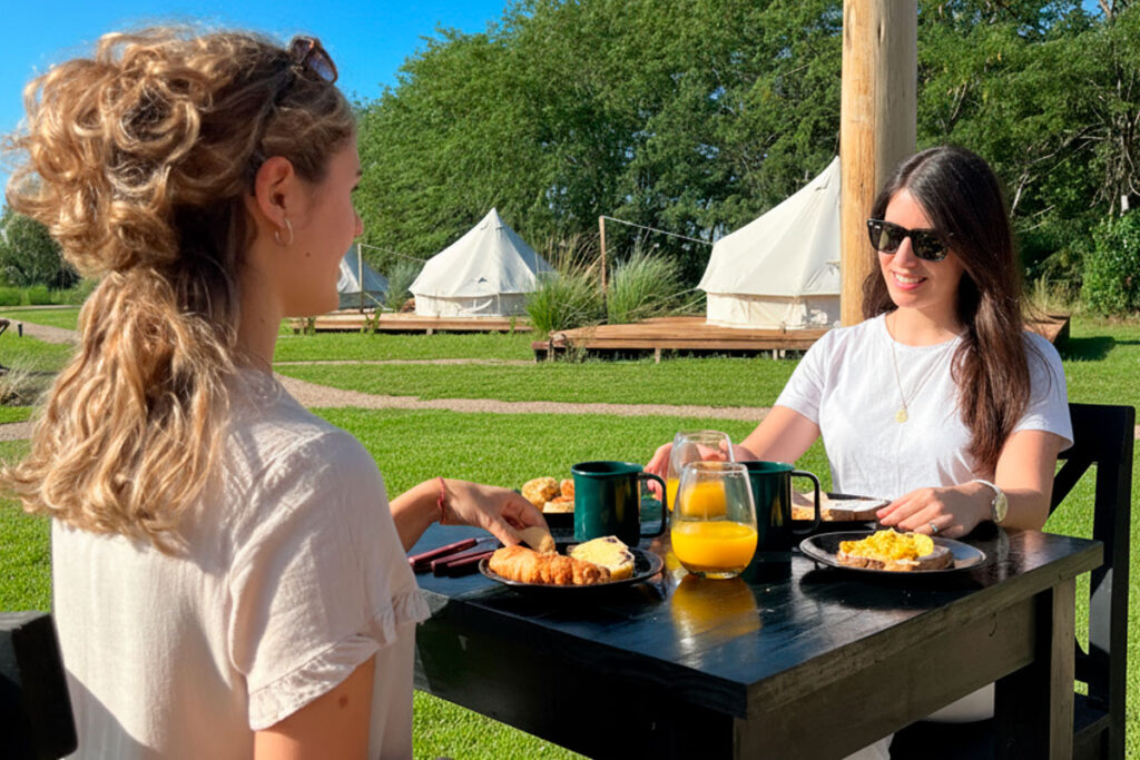 Dos mujeres disfrutando de un desayuno al aire libre con vistas a las carpas en Terranova Glamping.