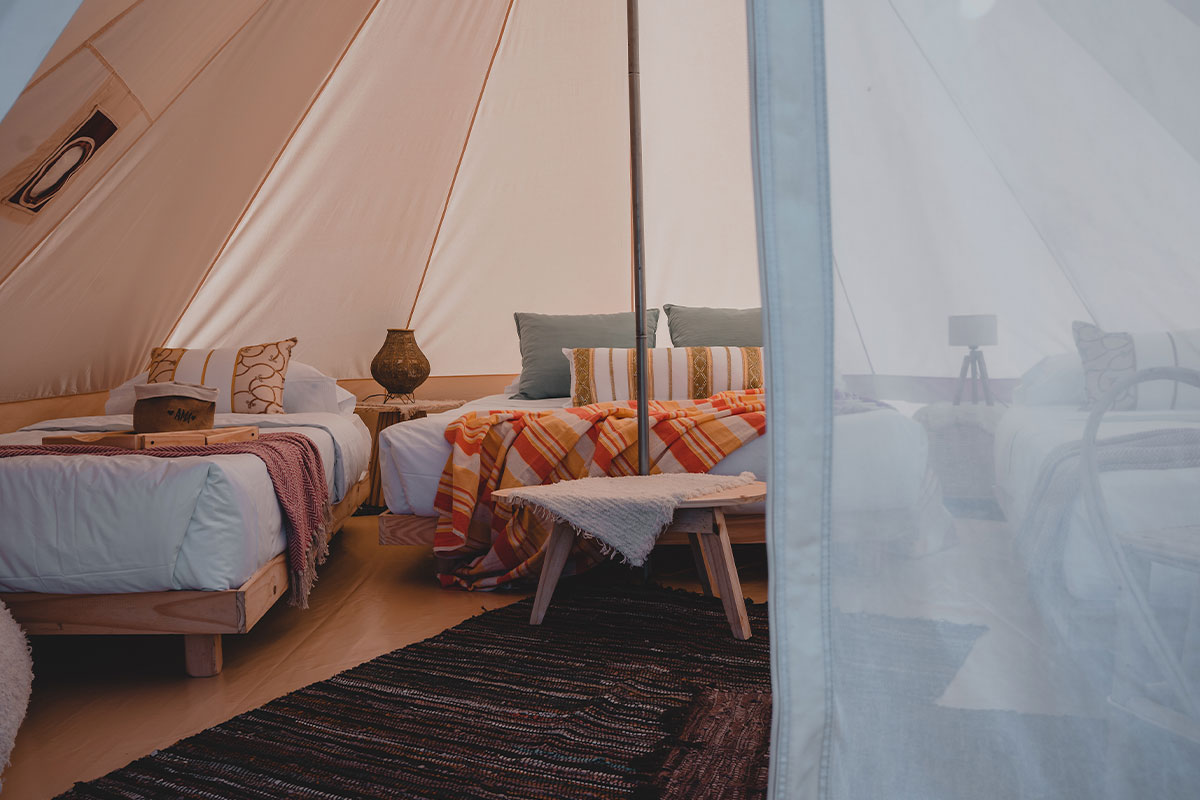 Interior de carpa de glamping con cama doble y cama individual, decoración rústica y confortable en Terranova.