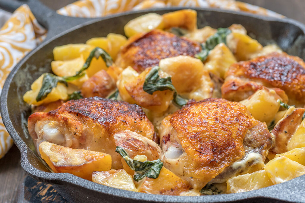 Cena gourmet "Noche a las Brasas" en Terra Nova Glamping: sartén de hierro con pollo asado, papas doradas y espinacas en salsa cremosa.